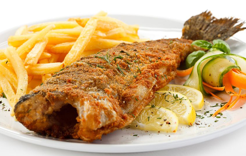 Whole breaded fried fish served with french fries, lemon slices, and vegetable garnish on a white plate
