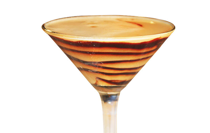 Martini glass with layered brown and cream cocktail in striped pattern, warm elegant tones