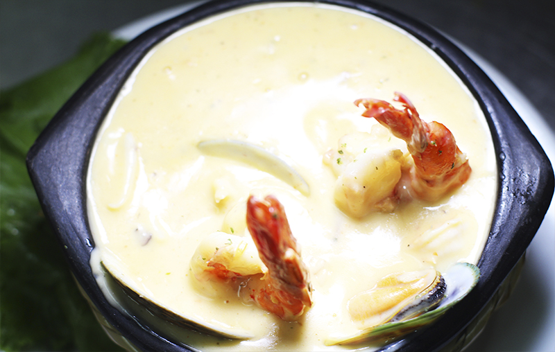 Dark bowl of creamy yellow soup with shrimp, mussels and other seafood, warm tones, rustic culinary mood